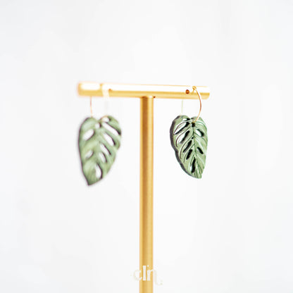 a pair of green leaf earrings hanging from a wooden stand