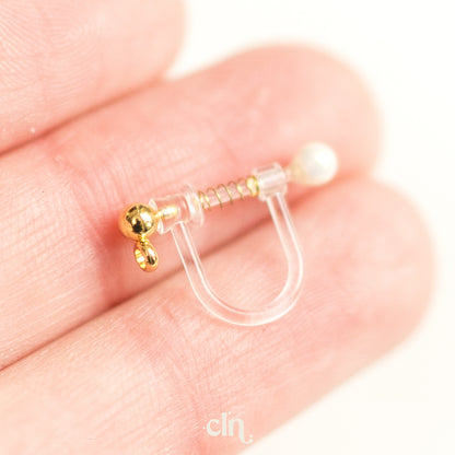 a person is holding a tiny gold and white nose ring